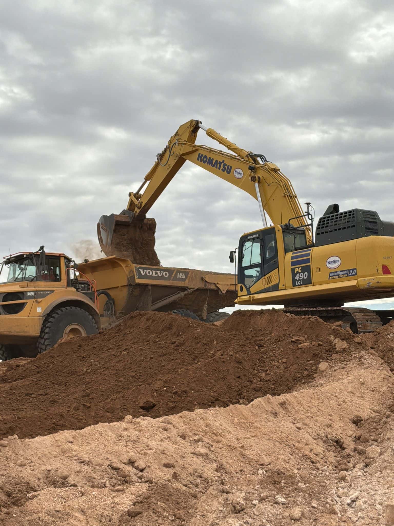 Excavator loading an articulated haul truck during cut work on a Midland, TX site