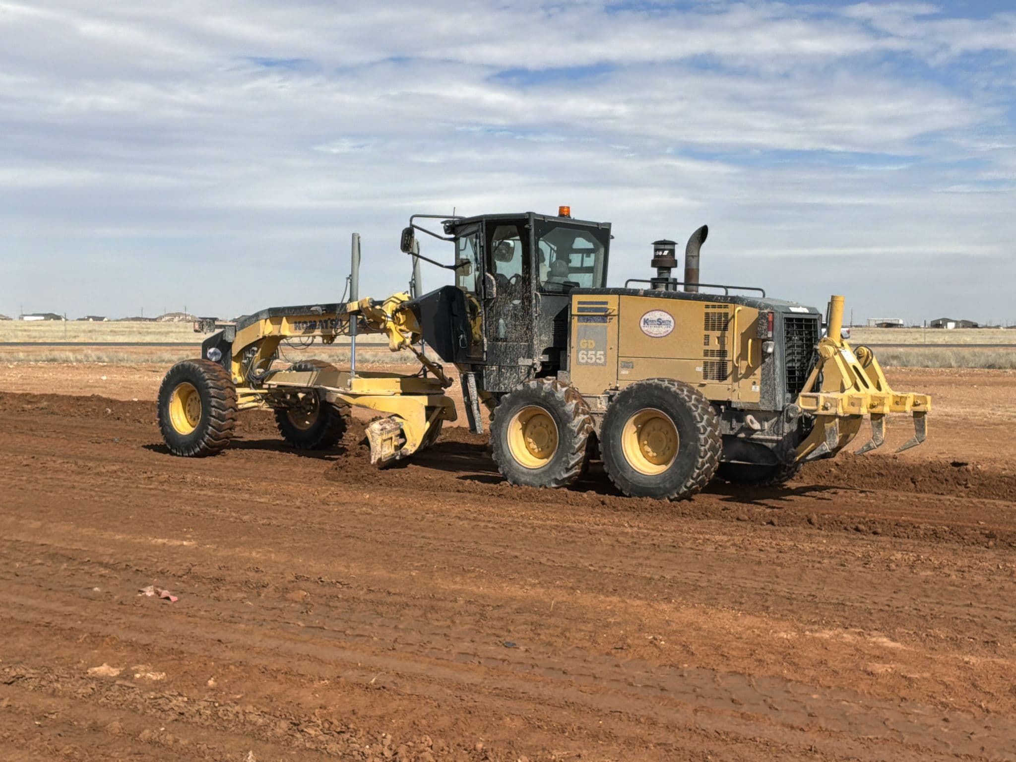 Motor grader with its scarifier down, ripping a pad surface before the next lift goes in