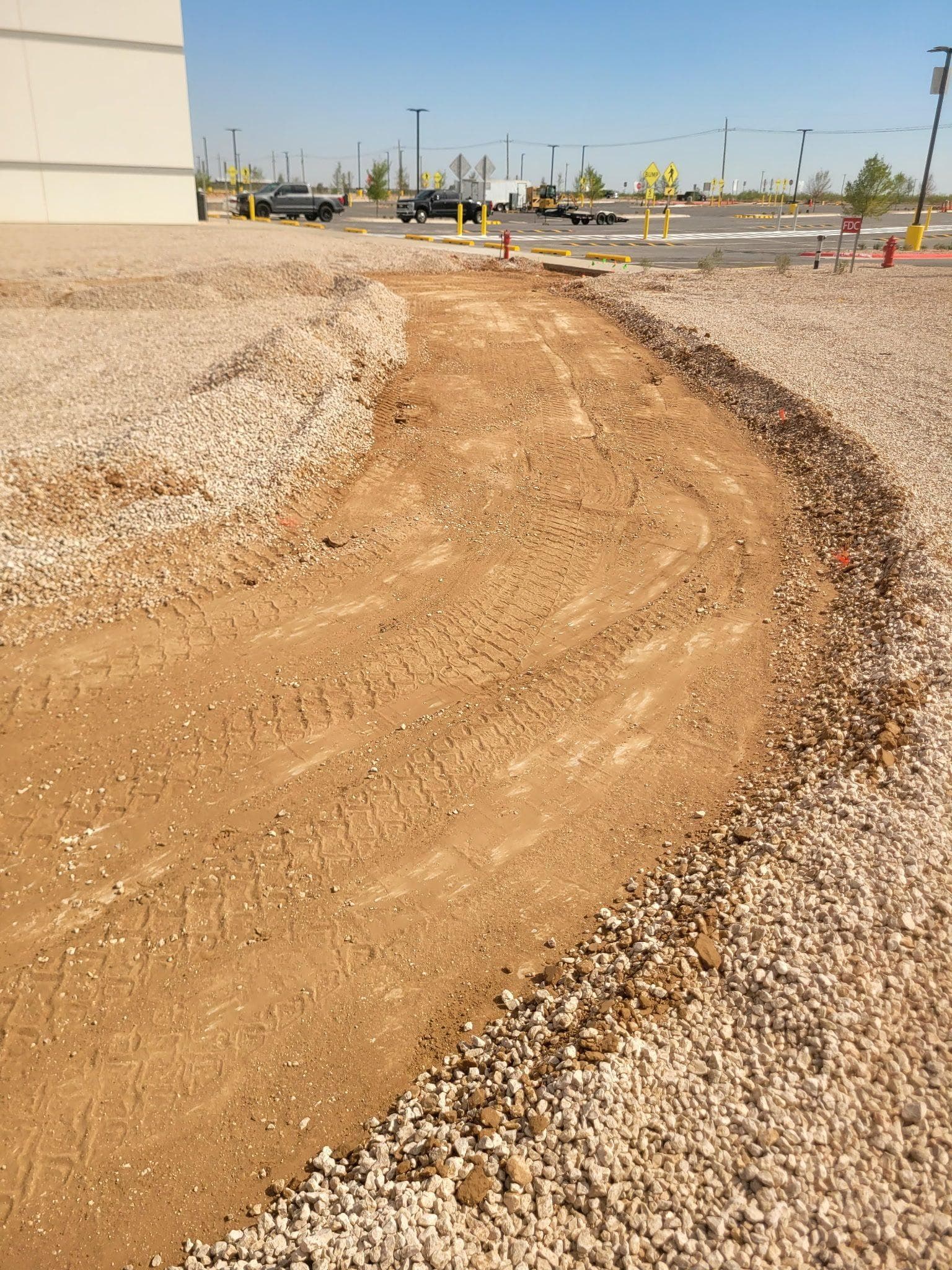Curved caliche driveway entrance edged with rock leading up to a shop building