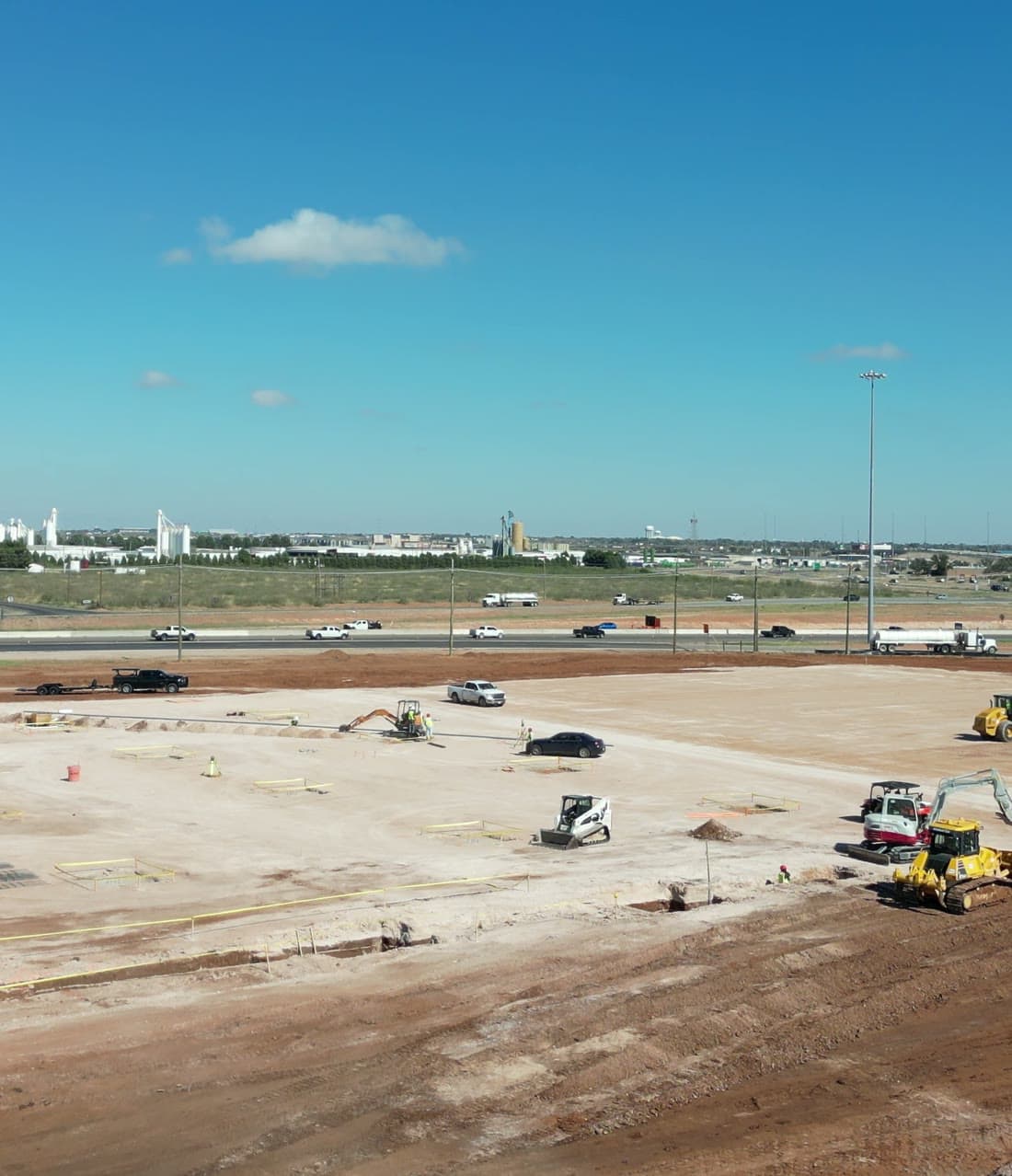 Aerial view of a large commercial pad site under construction in Midland, TX, with dozers, excavators, and skid steers working across the graded footprint