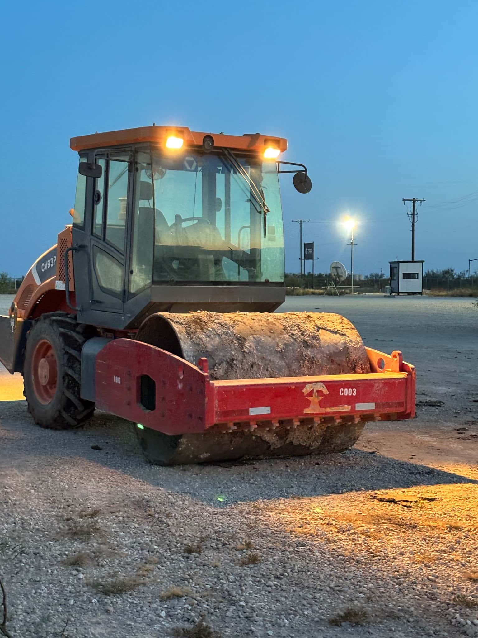Padfoot compactor caked in caliche at dusk with work lights on, Permian Basin jobsite