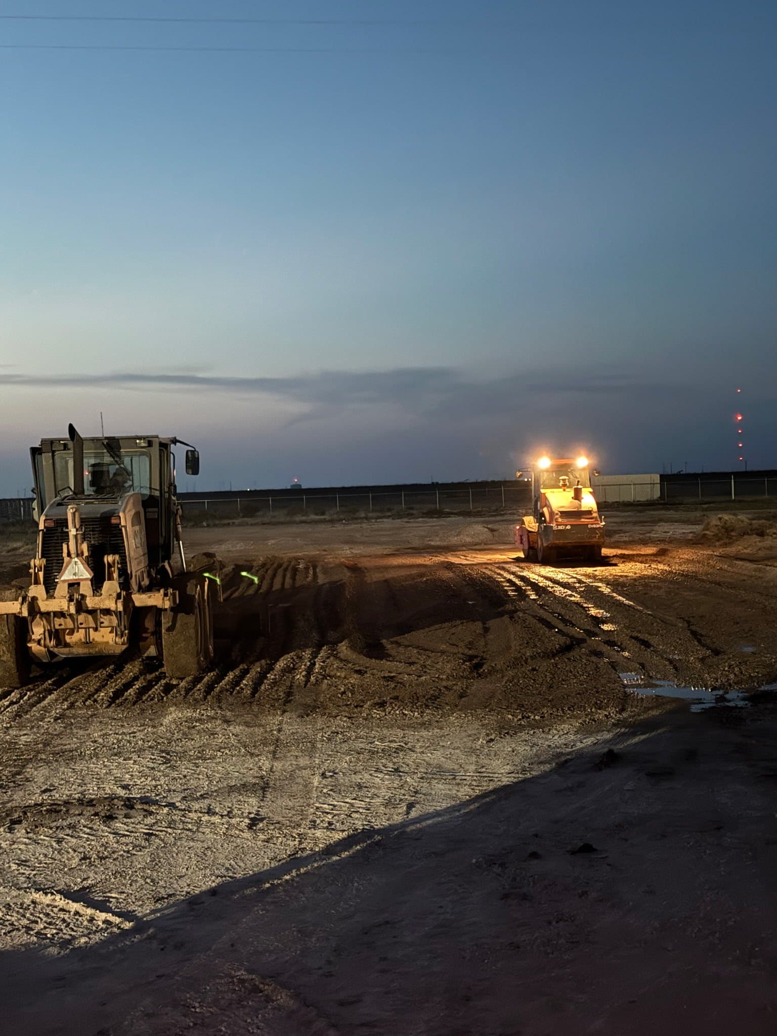 Motor grader and padfoot roller working a moisture-conditioned lift after dark