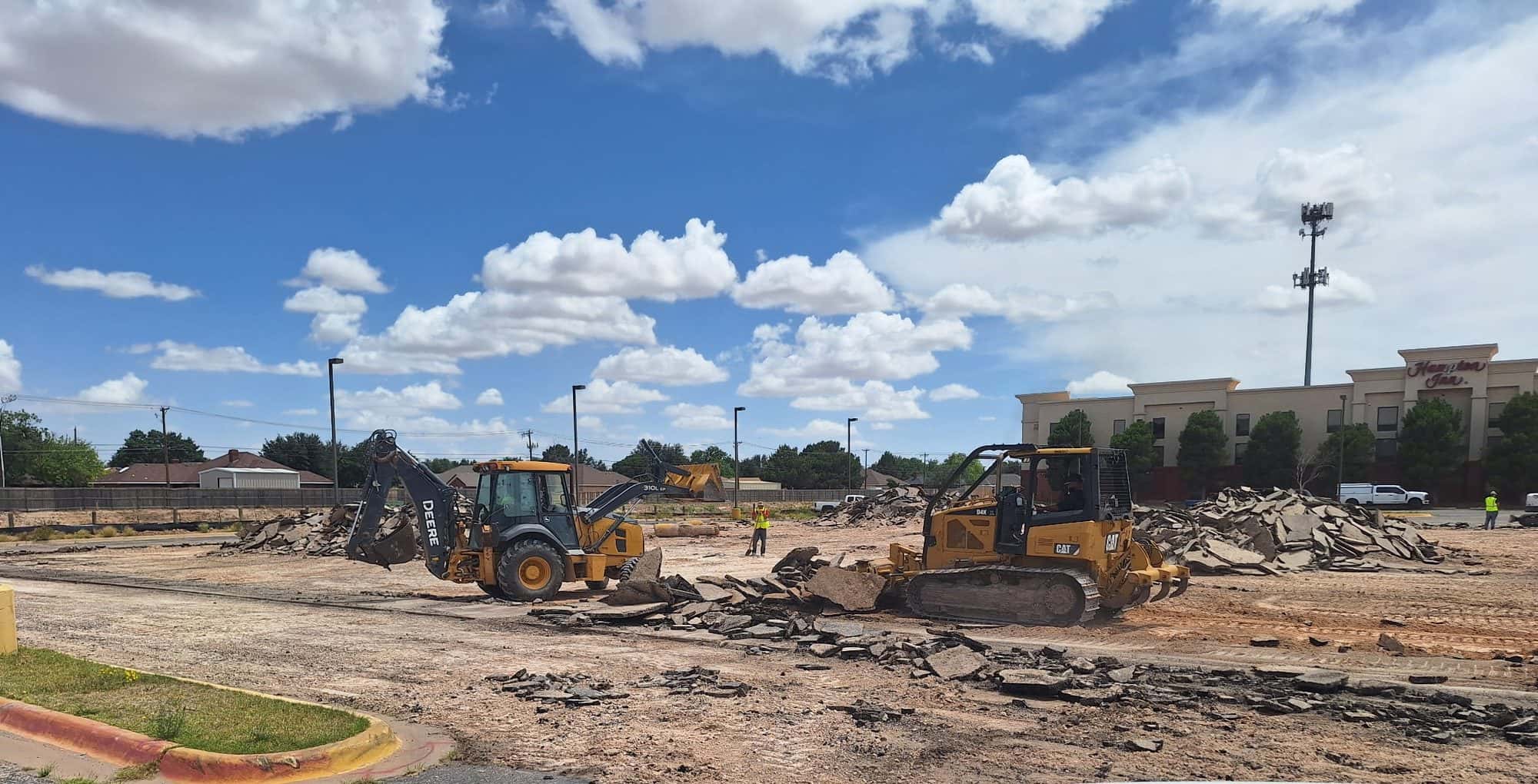 Backhoe and dozer breaking out a failed asphalt parking lot with broken material stockpiled for haul-off