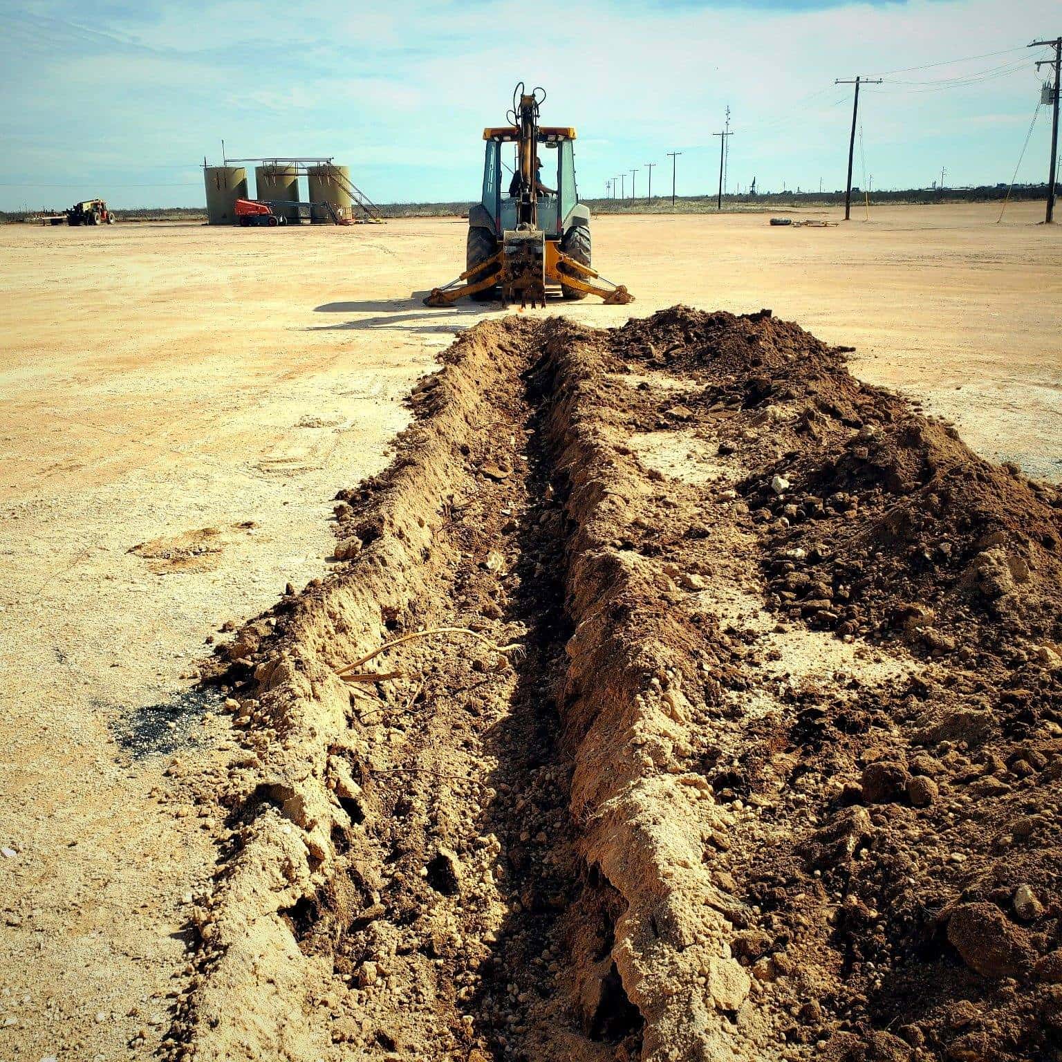 Backhoe digging a utility trench, ground-level view