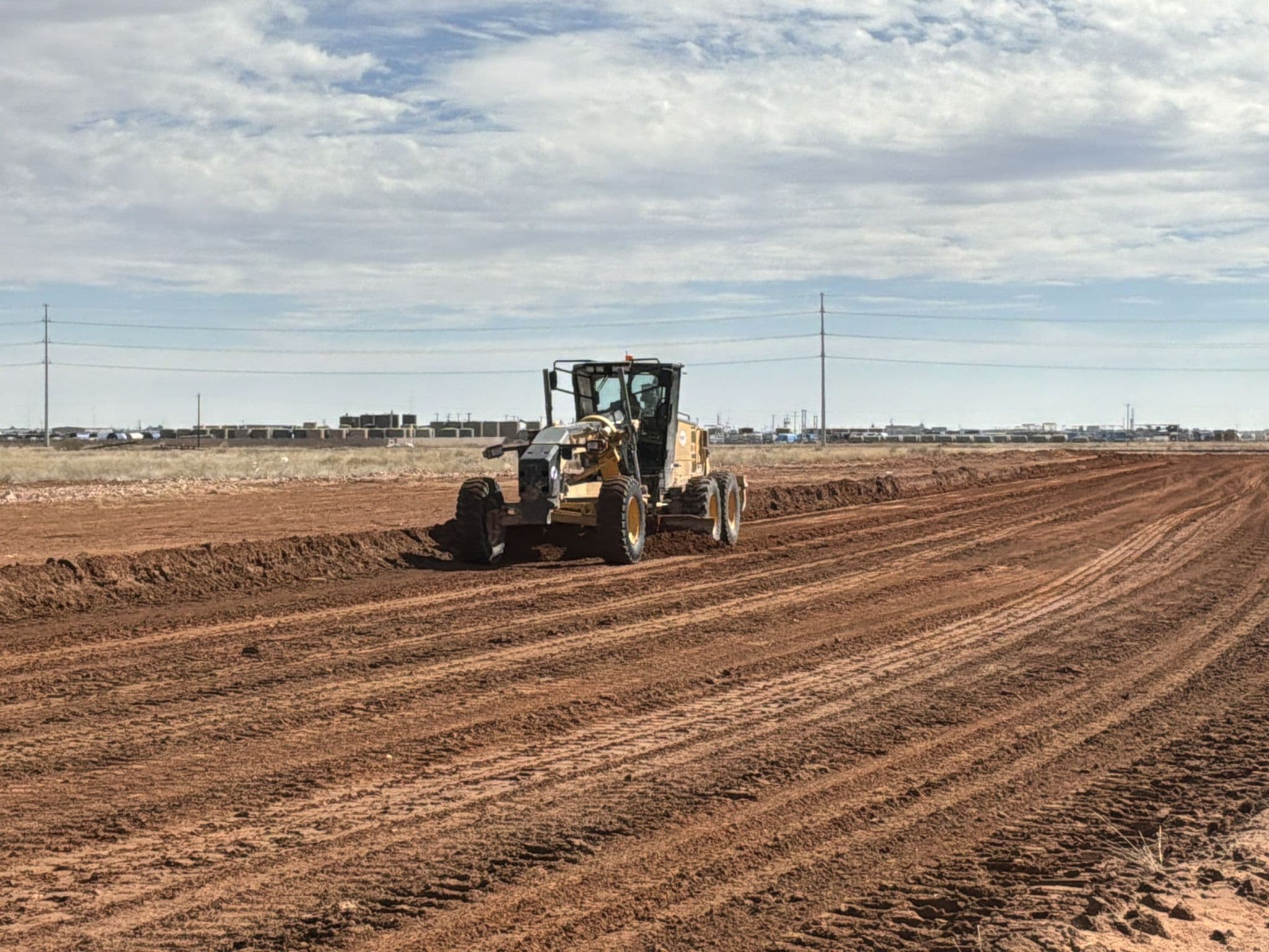 Motor grader shaping road subgrade in Midland, TX, the base layer a paved surface is built on