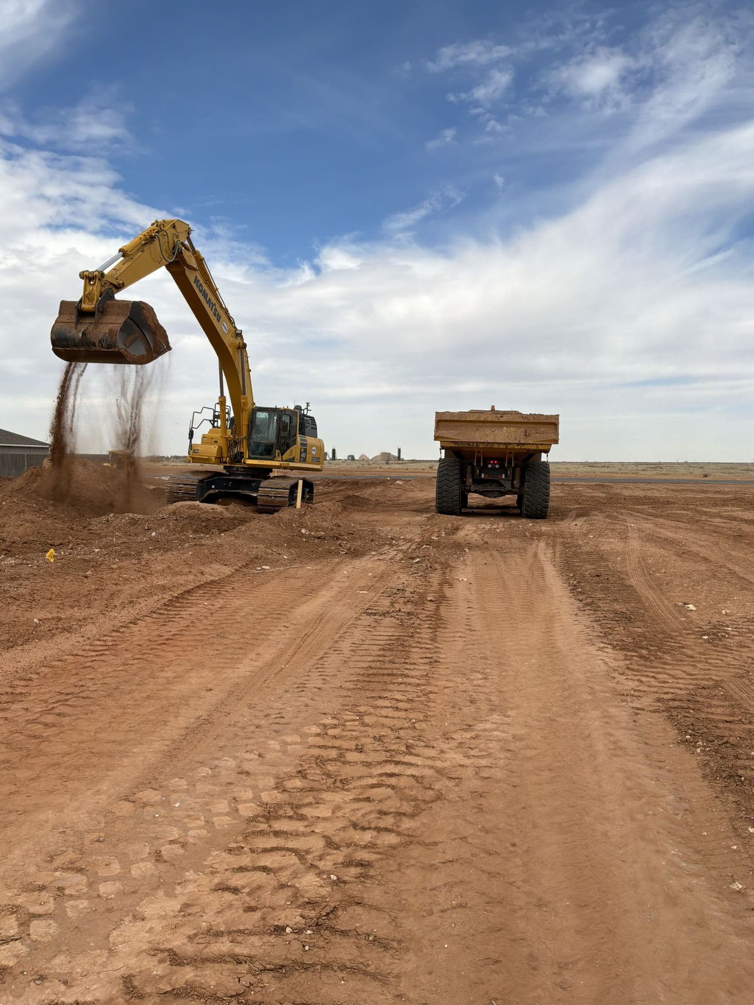 Excavator loading a haul truck on the site haul road during earthwork in Midland, TX