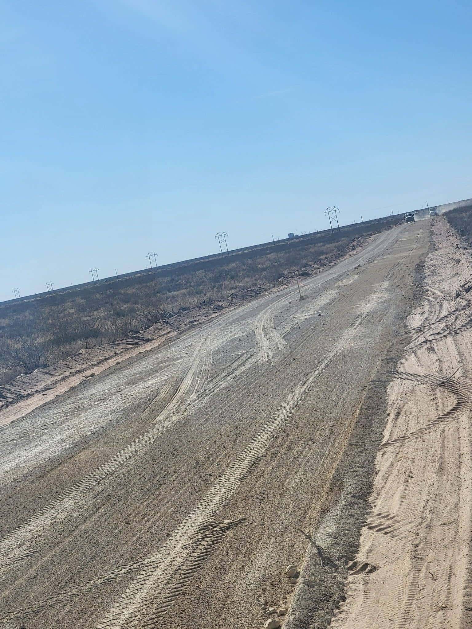Wide compacted caliche driveway with a center crown cut across Permian Basin ground